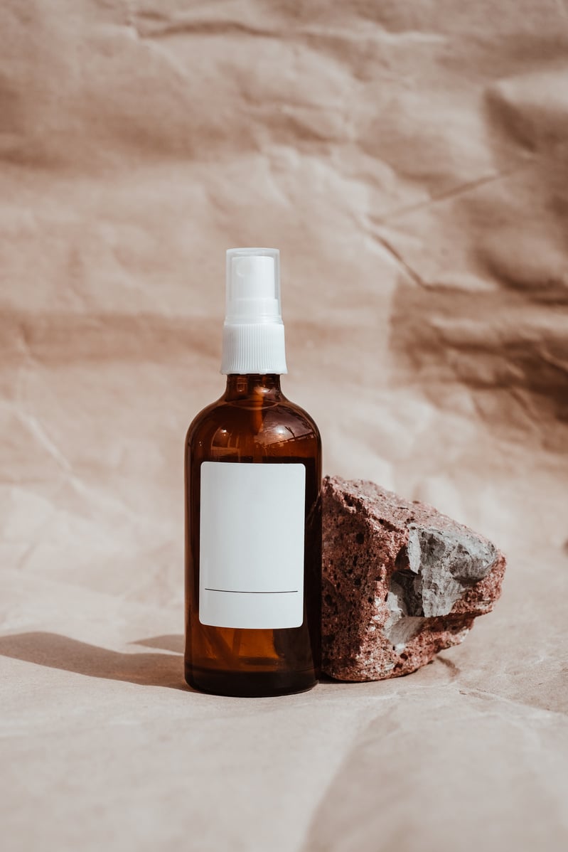 Spray Bottle Cosmetic Product and Rock on Brown Background